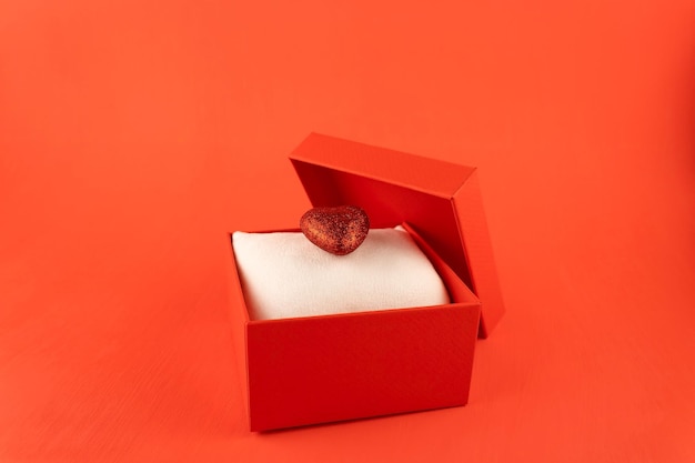 Caja de regalo roja con un corazón brillante sobre una almohada blanca sobre un fondo rojo.