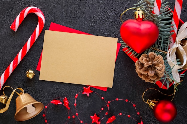 Caja de regalo roja con un juguete navideño en forma de corazón, una campana de oro, ramas de abeto, dulces navideños, guirnaldas y una tarjeta de texto de felicitación.