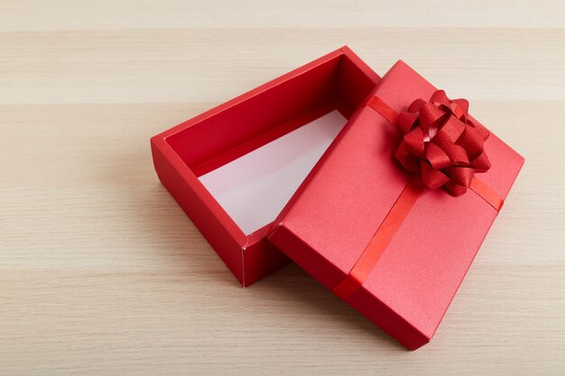 Caja de regalo roja con lazo de cinta abierta en mesa de madera blanca vintage