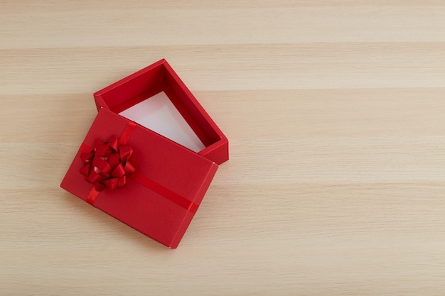 Caja de regalo roja con lazo de cinta abierta en mesa de madera blanca vintage