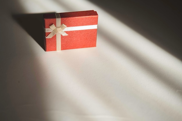 Caja de regalo roja con un lazo de cinta de luz sobre un fondo blanco.