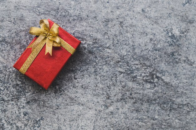 Caja de regalo roja y un lazo dorado colocado sobre una mesa de piedra gris.