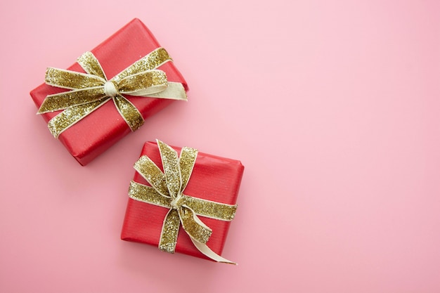 Caja de regalo roja y lazo dorado, sobre fondo rosa. Día de San Valentín, cumpleaños, concepto de fiesta.