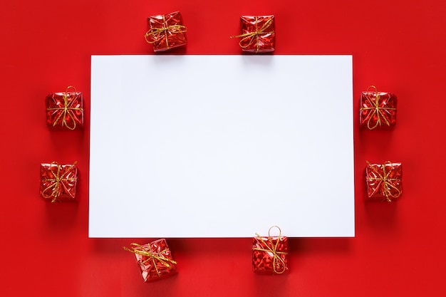 Caja de regalo roja y nota de papel vacía sobre fondo rojo.