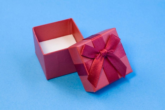 Caja de regalo roja vacía con lazo de cinta rojo oscuro de seda sobre fondo azul brillante