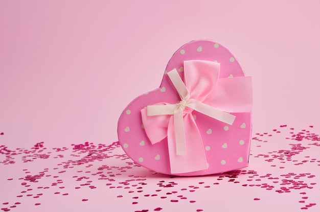 Caja de regalo rosa cerrada en forma de corazón con un lazo sobre un fondo rosa