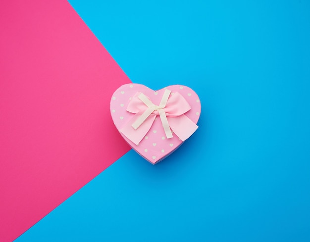Caja de regalo rosa en forma de corazón con un lazo sobre un fondo azul.