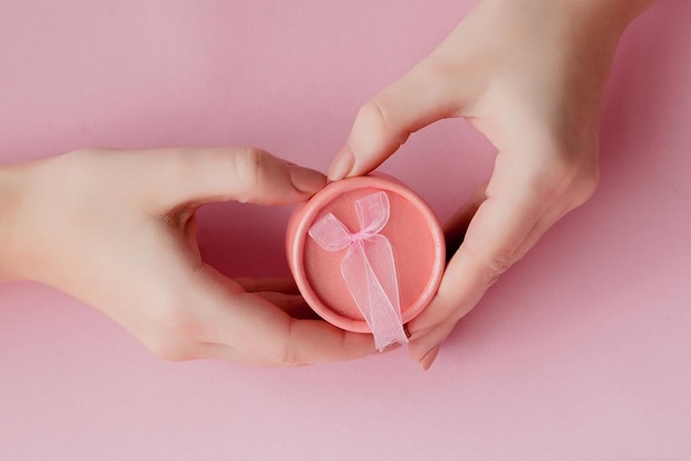 Caja de regalo rosa redonda en manos de mujeres sobre un fondo rosa Concepto festivo para el día de San Valentín Día de la madre o cumpleaños