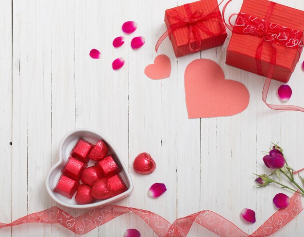 Caja de regalo de San Valentín y formas de corazón rojo sobre tabla de madera blanca