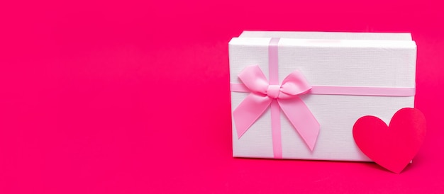 Foto caja de regalo y tarjeta en forma de corazón sobre fondo rosa-rojo. regala regalos con amor en san valentín, navidad y cumpleaños. envase blanco delicado con cintas. sorprende a tu amado. felices fiestas.