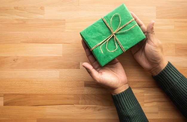 Caja de regalo verde en mano masculina sobre mesa de madera