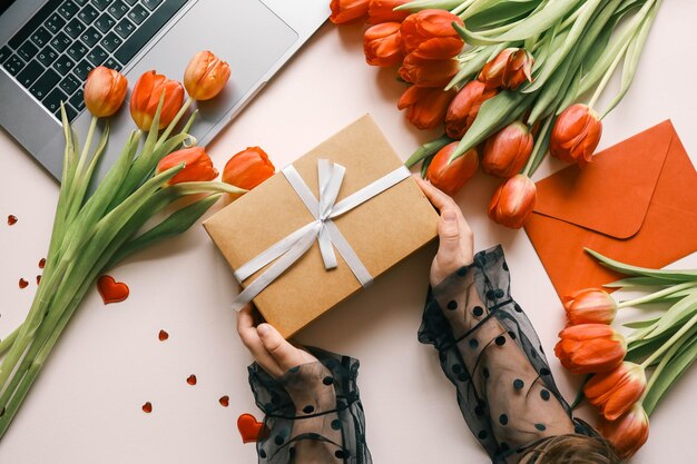 Caja de regalos con un arco y tulipanes en las manos de una chica de fondo festivo