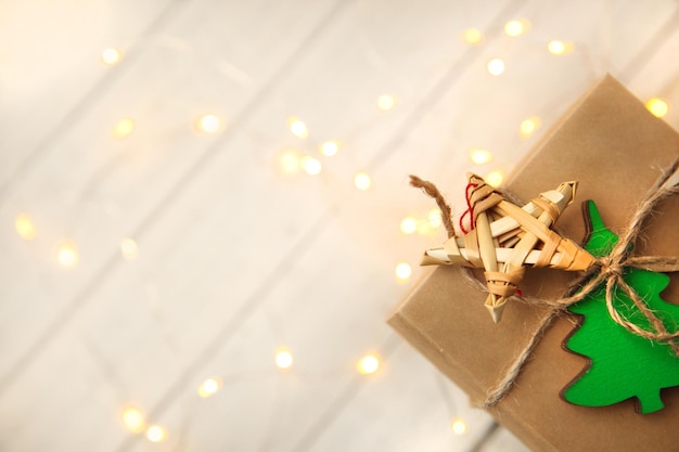 Foto la caja de regalos de artesanía está decorada con un árbol de navidad y una estrella de paja en un fondo de madera clara con luces borrosas