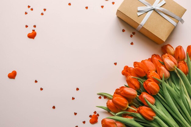 Caja de regalos con un lazo y un ramo de tulipanes rojos de fondo