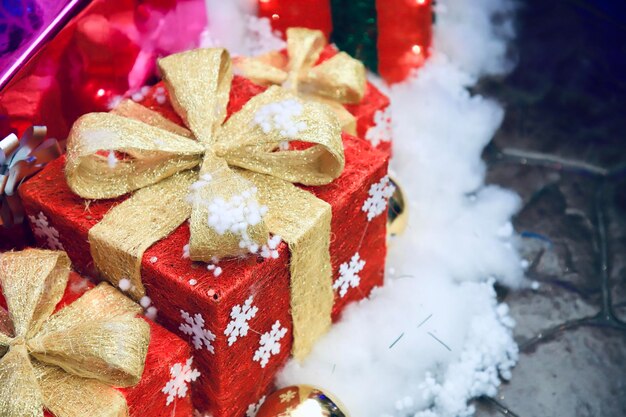 Una caja de regalos roja con un arco dorado en un piso de algodón blanco para decorar el lugar del año nuevo