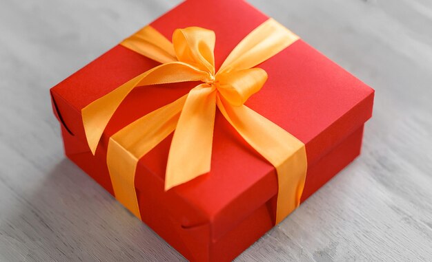 Caja roja atada con una cinta dorada. la cinta está atada a una caja en forma de un hermoso lazo. concepto de regalo de vacaciones