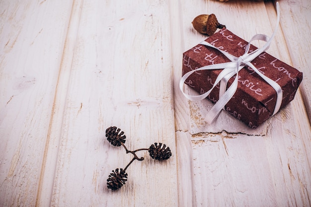 Caja roja presente, conos, canela y otra decoración rústica de Navidad en la mesa de madera