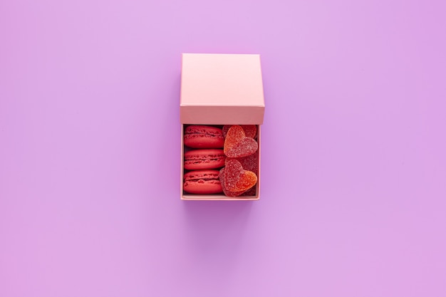Caja rosa con mermelada y macarrones y una hermosa rosa sobre una mesa rosa