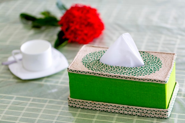 Caja de servilletas de fibra hecha a mano verde en la mesa del comedor con una flor roja.
