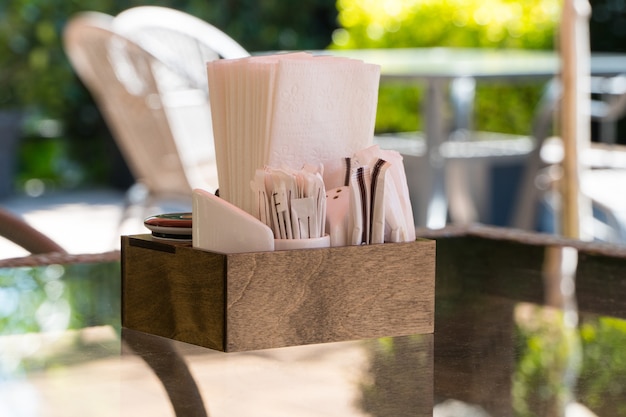 Caja con servilletas de papel sobre una mesa de vidrio, primer plano. parte del ajuste de la mesa café de verano al aire libre