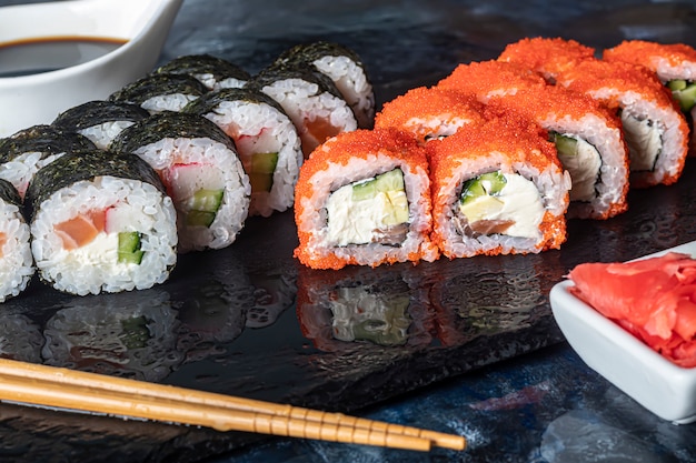 Una caja de sushi Nigiri, Uramaki California, Filadelfia, sobre una placa de piedra negra. Menú de sushi en una caja de transporte blanca sobre un fondo de madera.