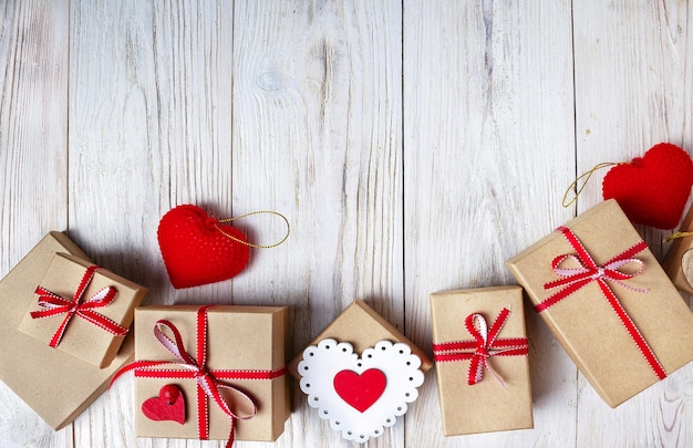 Cajas artesanales atadas con cintas rojas y corazones rojos se encuentran en un espacio de copia de fondo de madera blanca