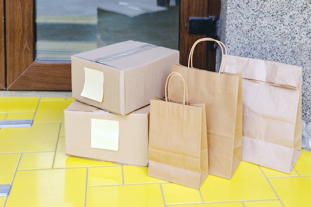 Cajas de entrega, bolsas de papel en la puerta cerca de la puerta de su casa. Entrega de comida sin contacto. Compras seguras Comercio electrónico compra paquetes a domicilio. Cajas entregadas a la puerta de entrada por mensajería, cartero.