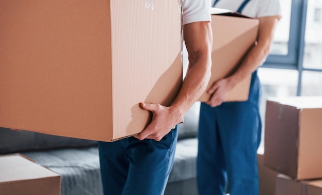 Con cajas en las manos Dos jóvenes motores en uniforme azul trabajando en el interior de la habitación