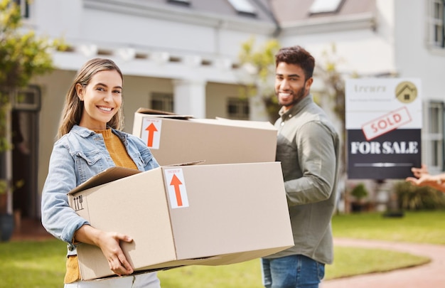 Foto cajas de pareja y retrato para casa nueva bienes raíces y propiedad propietario de casa y vecindario al aire libre personas interraciales jóvenes y felices con cartón moviéndose en la casa de ensueño juntos y vendido cartel