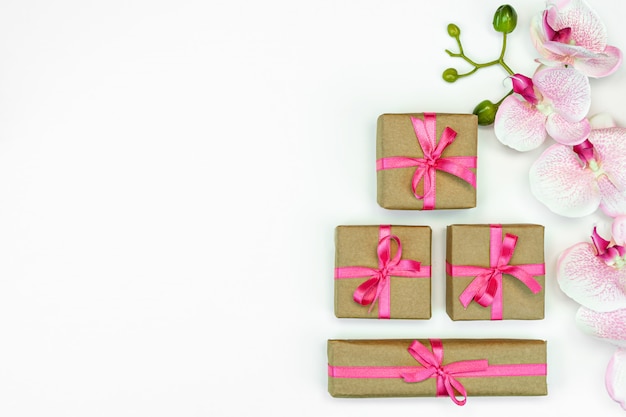 Foto cajas presentes con cinta rosa con flores de orquídeas sobre fondo blanco.