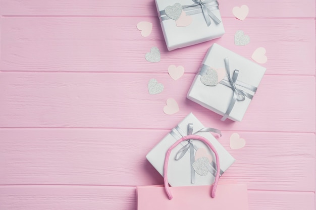Cajas de regalo blancas con cinta de raso plateada en paquetes rosas y confeti en forma de corazón