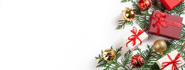 Cajas de regalo con cinta roja y bolas de Navidad doradas sobre un fondo blanco.