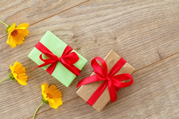 Cajas de regalo con cintas rojas y hermosas flores de caléndula en el fondo de madera. Concepto de dar un regalo en vacaciones. Vista superior.