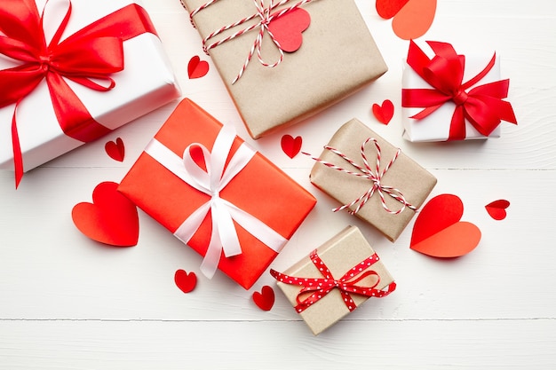 Cajas de regalo del día de San Valentín y corazones de papel rojo sobre mesa de madera blanca