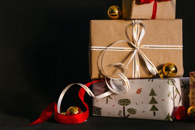 Cajas de regalo empaquetadas en papel de regalo y atadas con cintas para el año nuevo o Navidad están sobre un fondo negro, junto a ellas hay bolas navideñas doradas. preparándose para las vacaciones.