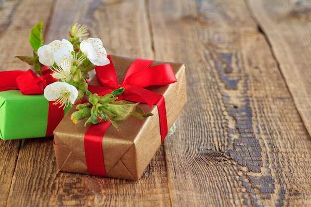 Cajas de regalo envueltas con cintas rojas decoradas con flores de jazmín sobre tablas de madera.