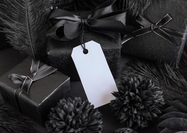 Cajas de regalo envueltas con flores y decoraciones de papel negro y maqueta de etiqueta de regalo vertical