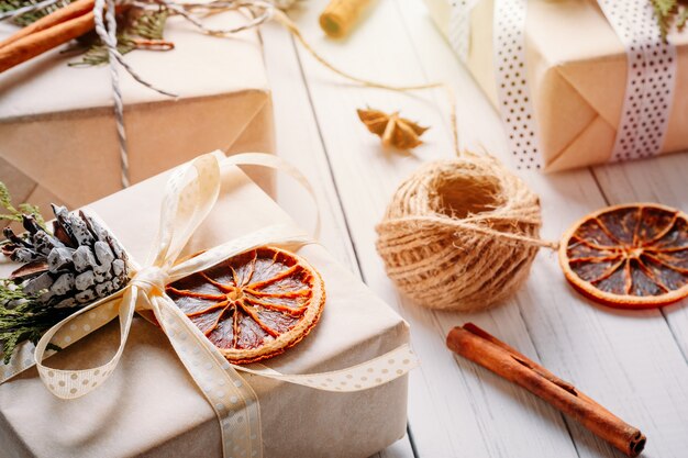 Cajas de regalo envueltas en papel con cintas, piñas y naranjas secas