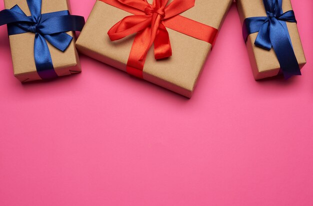 Cajas de regalo envueltas en papel marrón y atadas con un lazo rojo y azul, regalos sobre un fondo rosa, lugar para texto