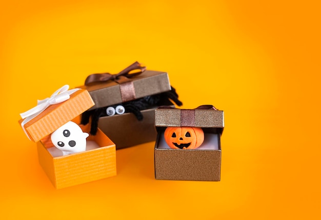 cajas de regalo con fantasma, calabaza y araña en primer plano de fondo naranja