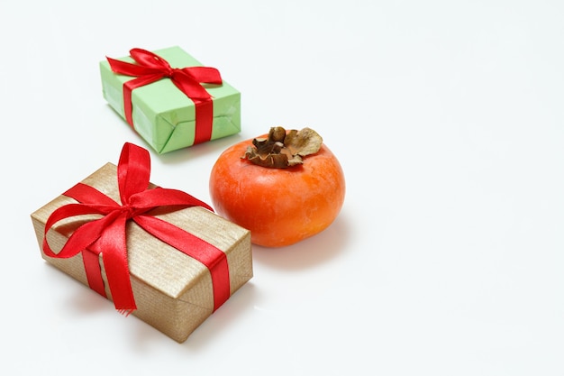 Cajas de regalo y una fruta de caqui madura sobre la superficie blanca