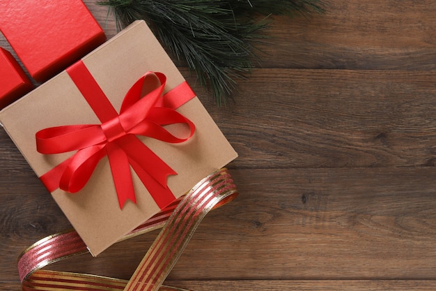 Cajas de regalo marrón y rojo y cinta roja sobre mesa de madera