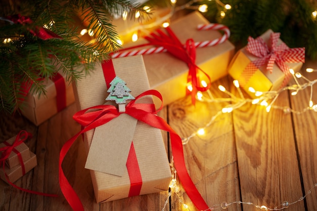 Cajas de regalo de Navidad en envases artesanales sobre una mesa de madera contra el árbol de Navidad. Cajas de regalo hechas a mano. Vacaciones de Navidad acogedor, concepto de estado de ánimo.