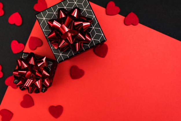 Cajas de regalo negras con motivos geométricos, decoradas con lazos rojos, sobre un fondo negro y rojo con