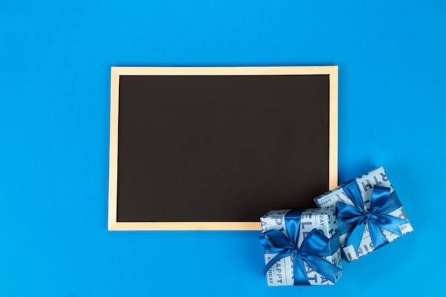 Foto cajas de regalo y pizarra sobre fondo azul con espacio de copia.