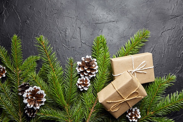 Cajas de regalo y rama de árbol de Navidad verde con cono sobre fondo oscuro vista superior