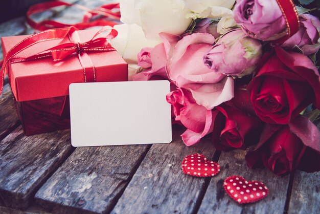 Las cajas de regalo rojas, los corazones rojos y las rosas se colocan en un piso de madera.