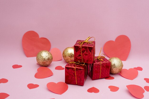 Cajas de regalo rojas, globos dorados y corazones rojos sobre un rosa.