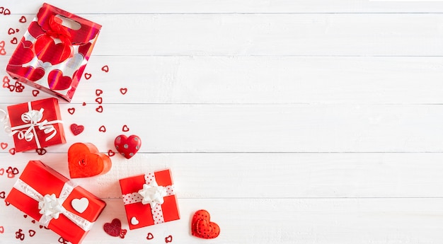 Foto cajas de regalo rojas y pequeñas decoraciones de corazón sobre fondo blanco de madera