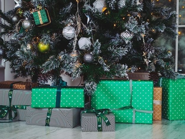 Cajas de regalo verde debajo de un árbol de Navidad decorado con juguetes de colores